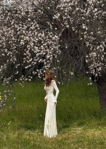 Woman in a white dress standing in a field with blooming trees