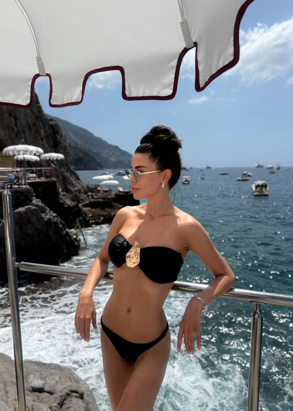 Woman in a black bikini standing by the ocean with a scenic background