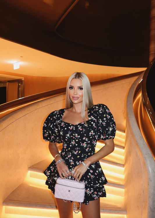 Woman in a floral dress holding a pink handbag in an elegant interior setting