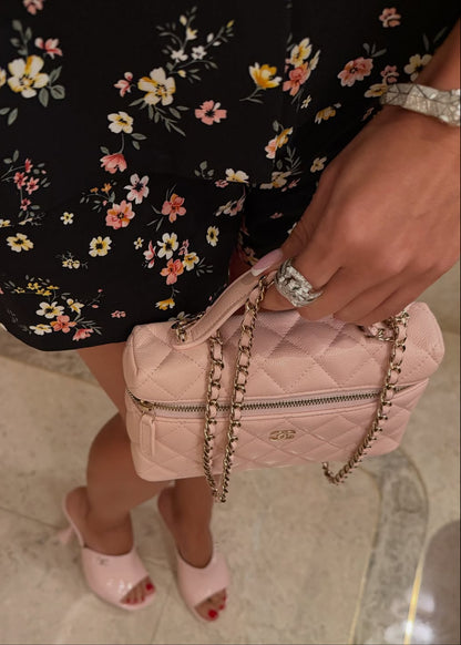 Person holding a pink quilted handbag with floral dress and high heels in the background