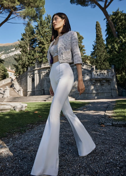 Woman in a stylish outfit standing in a scenic outdoor setting with trees and architecture.