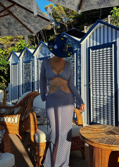 Person wearing a blue patterned dress and hat in an outdoor setting with wicker furniture and beach huts.