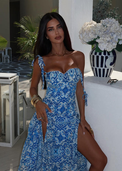 Woman in a blue patterned dress standing outdoors with decorative elements.