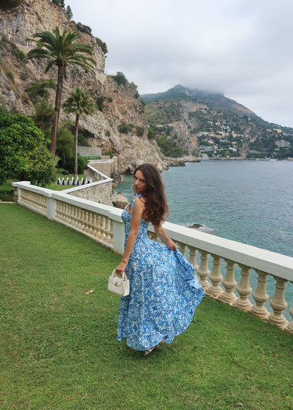 Woman in a blue floral dress standing on a grassy area with a scenic ocean view.