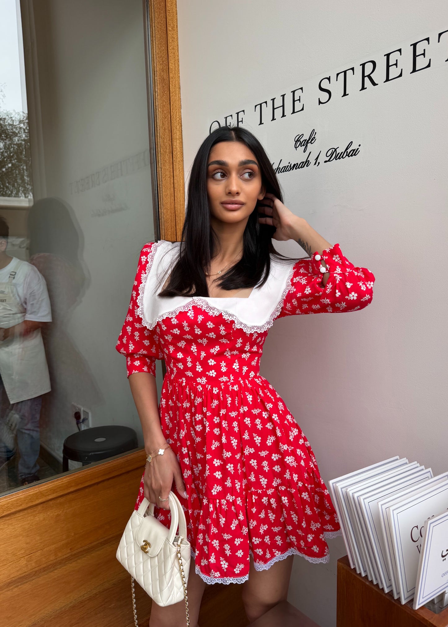Woman in a red floral dress standing in front of a 'Off The Street' sign.