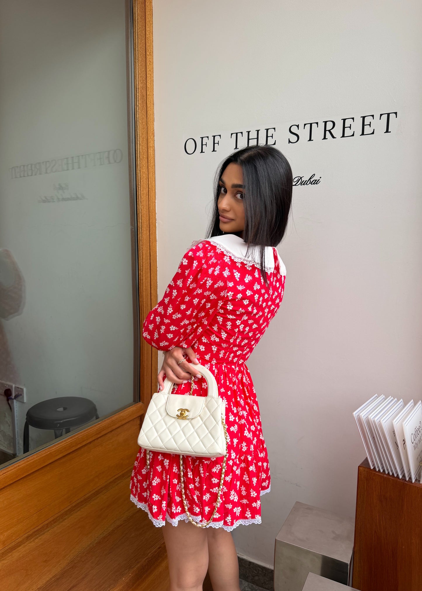 Woman in a red dress holding a white handbag in front of a 'Off The Street' store.