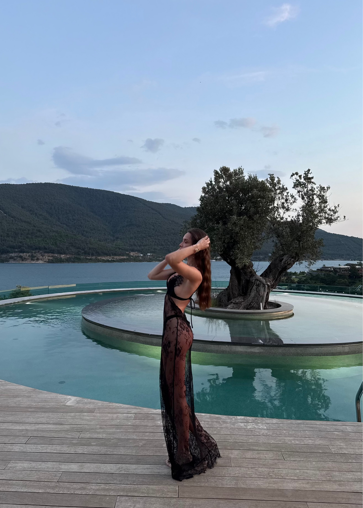 Woman in a black dress standing by a pool with a scenic background