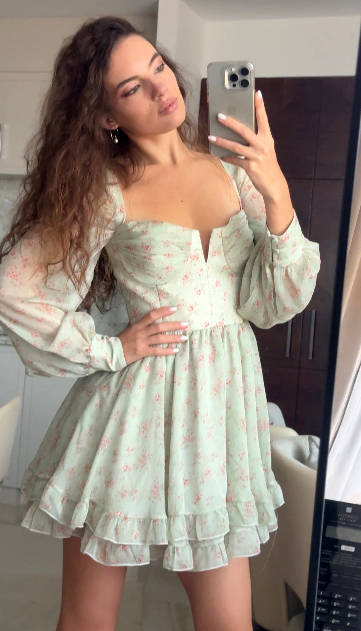 Woman taking a mirror selfie wearing a light green floral dress.