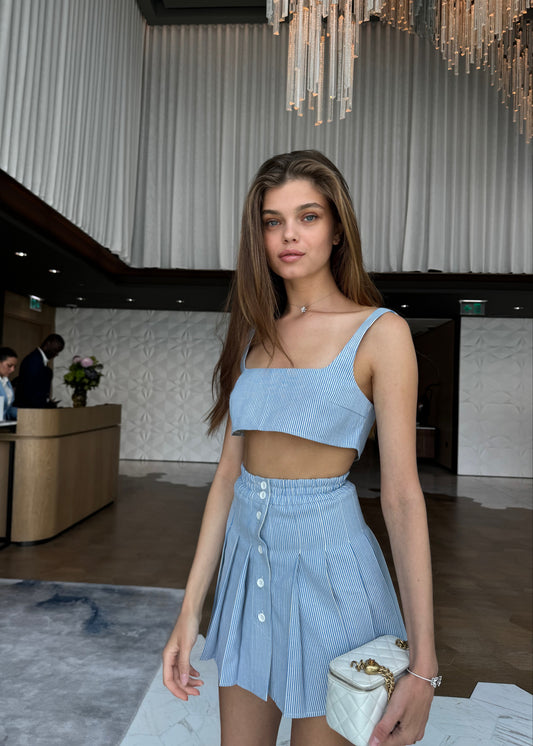 Woman in a light blue outfit standing in an indoor setting with a chandelier.