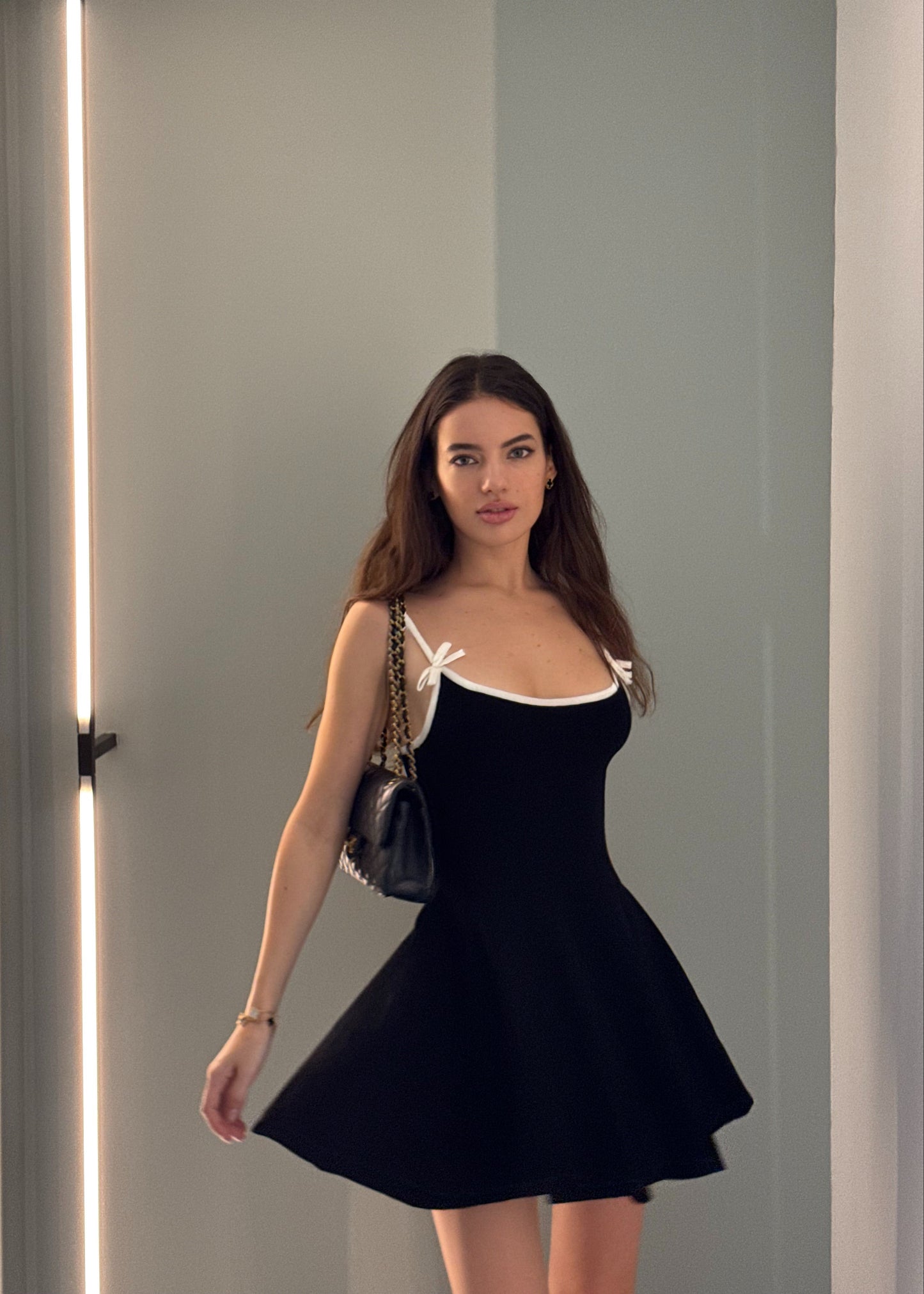Woman wearing a black dress with a white bow detail, standing against a plain background.