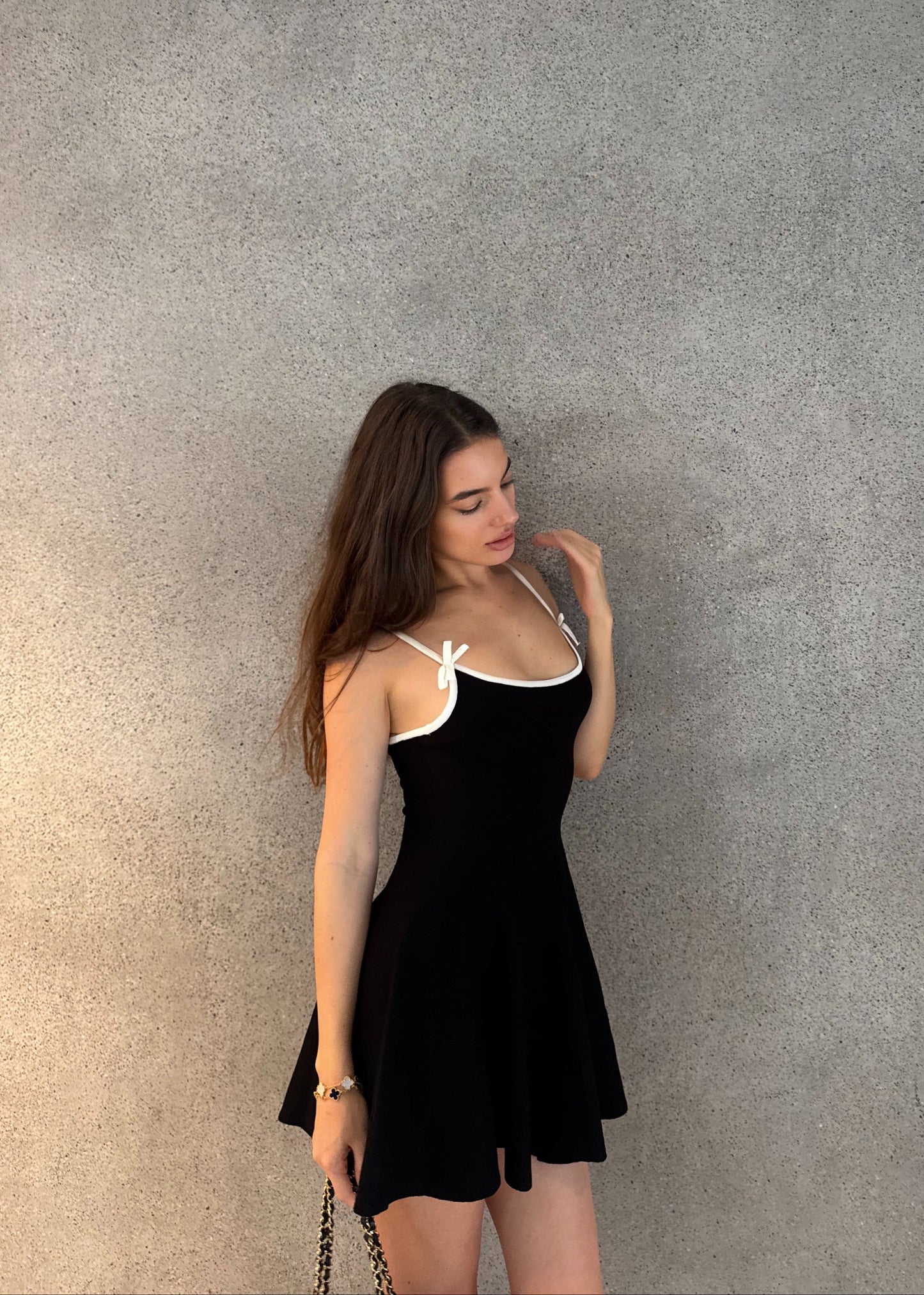 Woman wearing a black dress with white straps against a gray wall