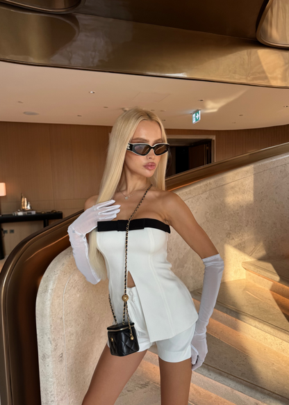 Woman in a stylish outfit with gloves and sunglasses in an elegant interior setting