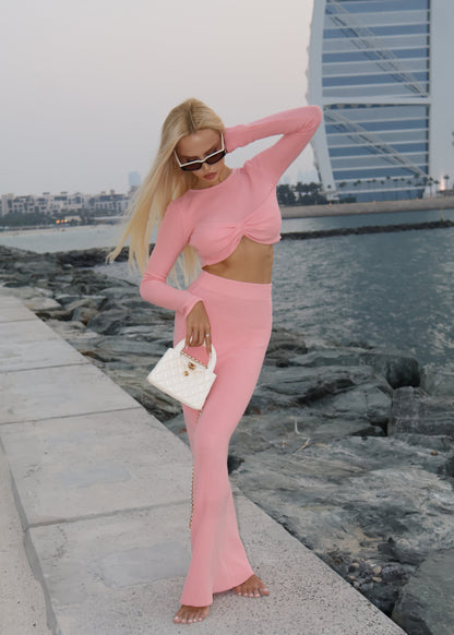 Woman in a pink outfit standing by a waterfront with buildings in the background