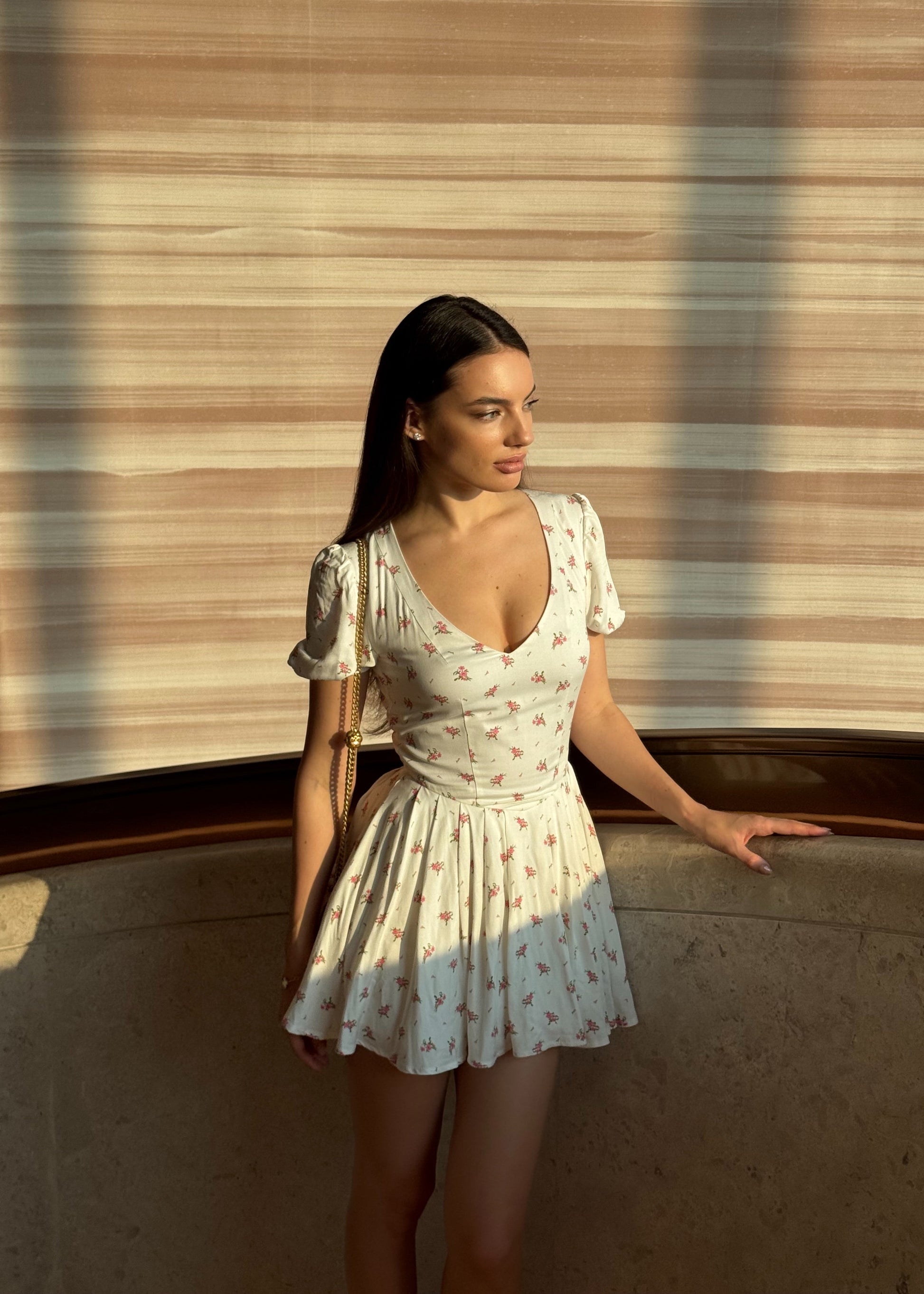 Woman in a white floral dress standing against a textured wall.