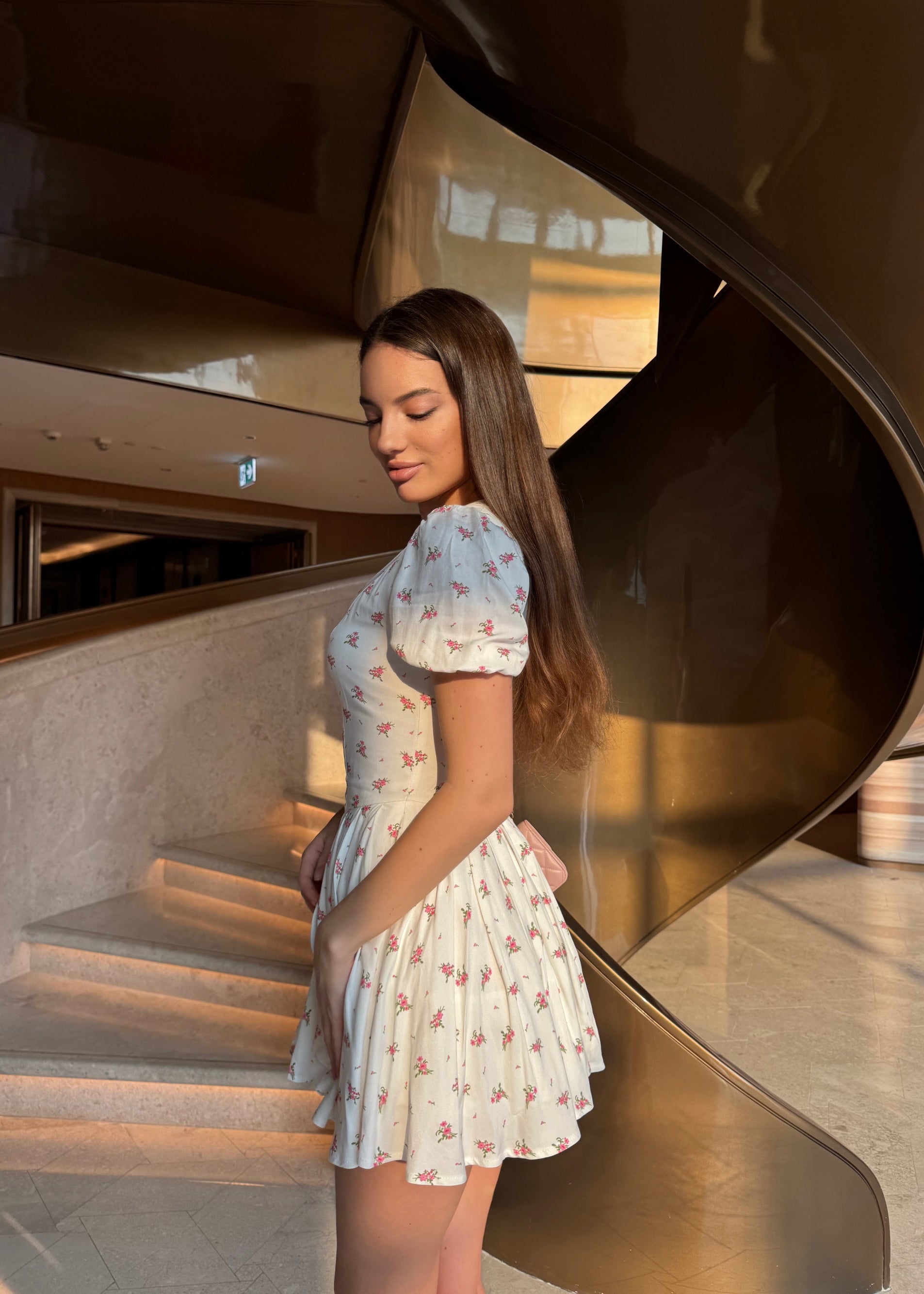 Woman in a floral dress standing next to a modern architectural structure.