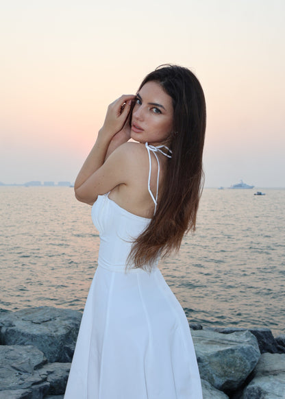 Woman in a white dress standing by the water with a sunset background