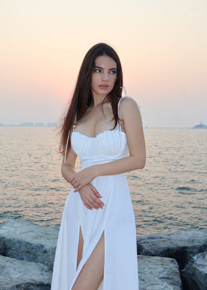Woman in a white dress standing by the sea at sunset