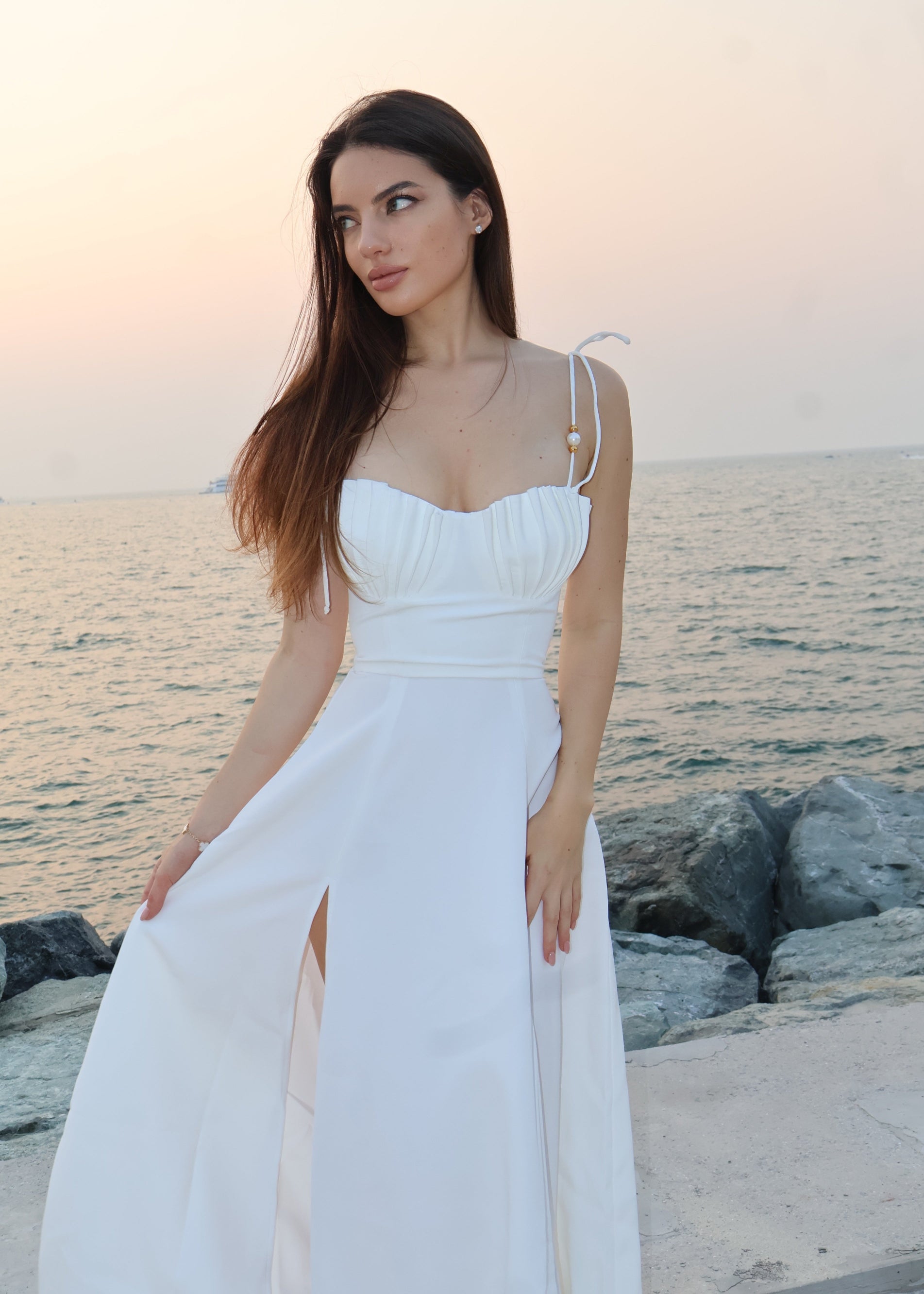 Woman in a white dress standing by the ocean at sunset