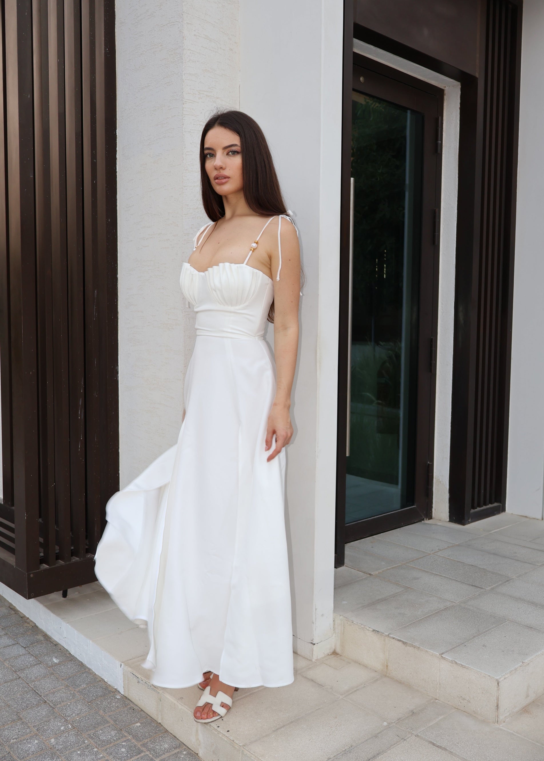 Woman in a white dress standing against a building entrance.