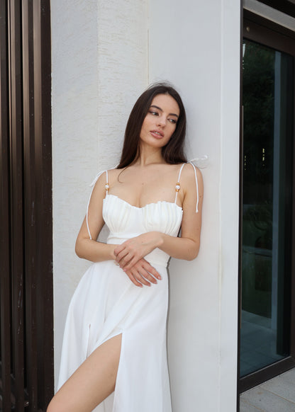 Woman in a white dress standing against a white wall.