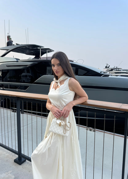 Woman in a white dress standing on a balcony with a yacht in the background