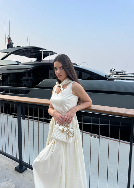 Woman in a white dress standing on a balcony with a yacht in the background
