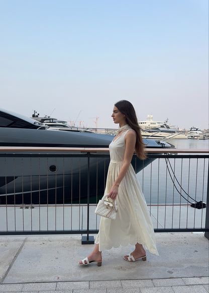 Woman in a white dress standing by a waterfront with yachts in the background