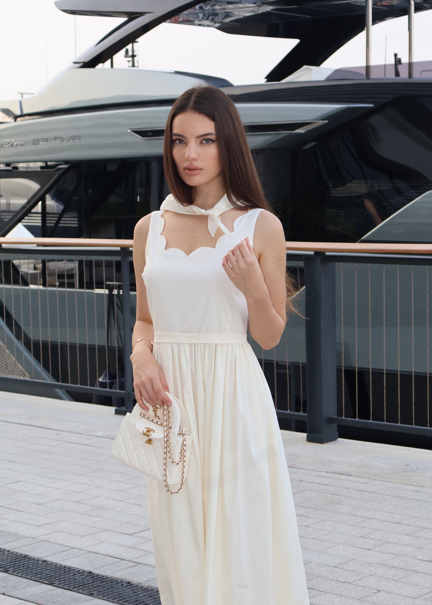 Woman in a white dress standing on a dock with a yacht in the background