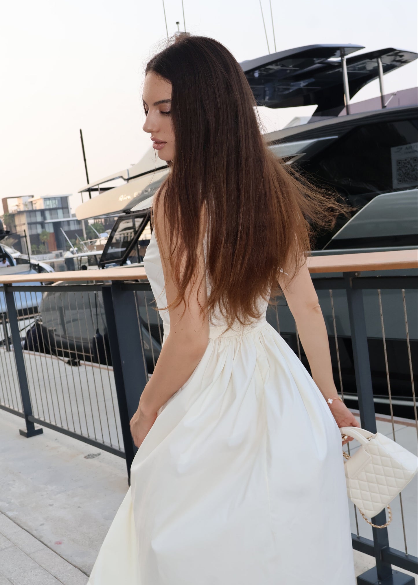 Woman in a white dress standing on a dock with yachts in the background