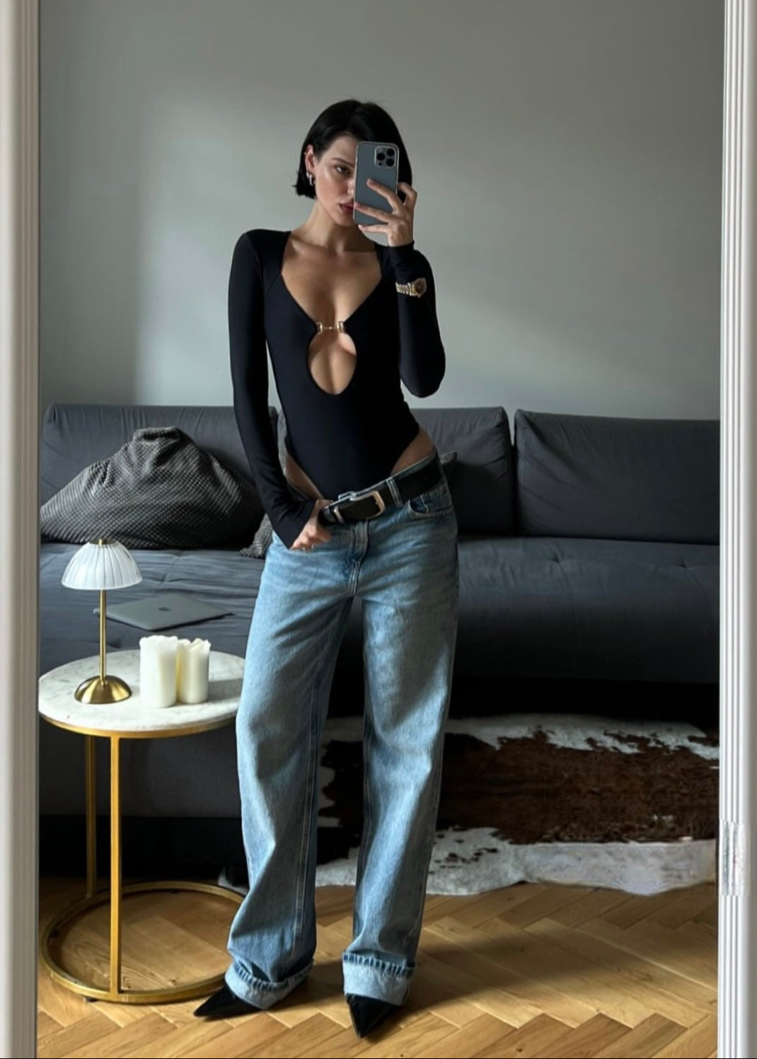 Person taking a mirror selfie in a living room with a gray couch and side table.