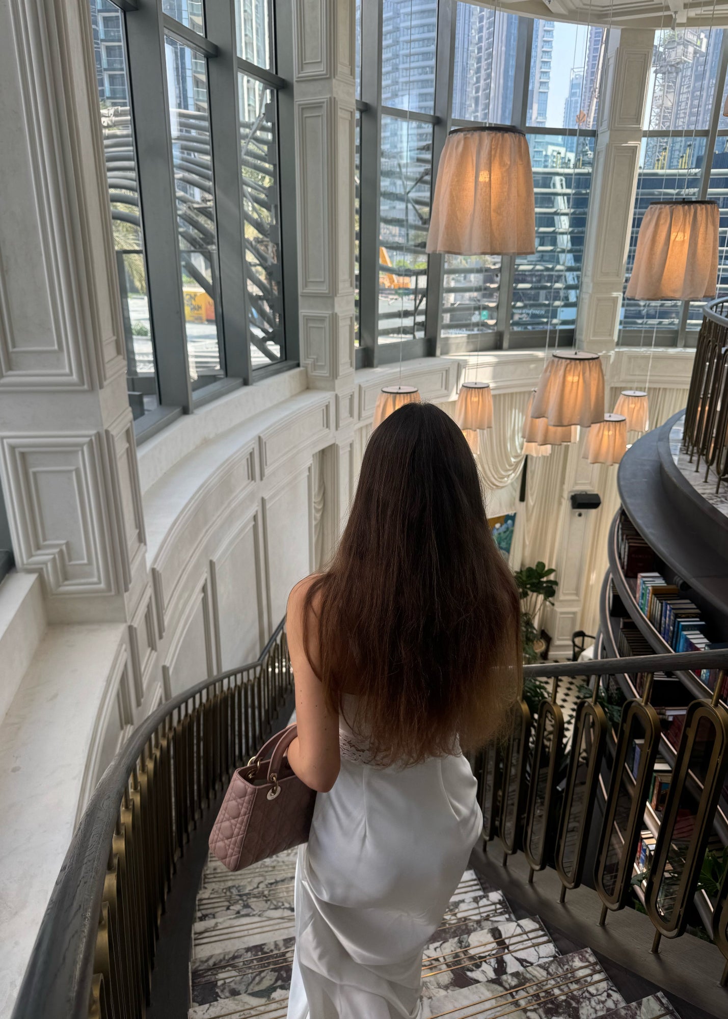 Woman in a white dress standing in a luxurious interior setting with high ceilings and large windows.