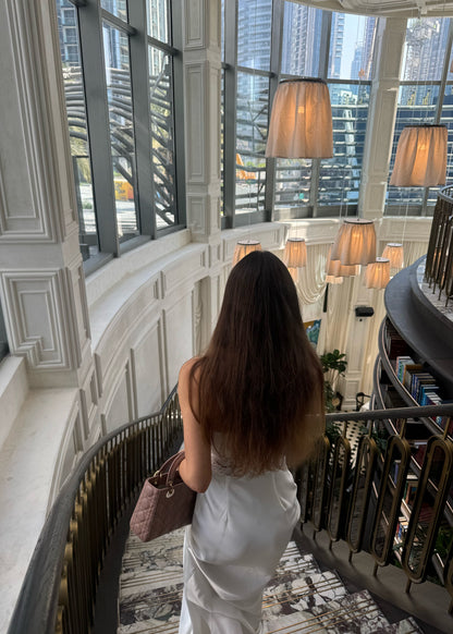 Woman in a white dress standing in a luxurious interior setting with high ceilings and large windows.